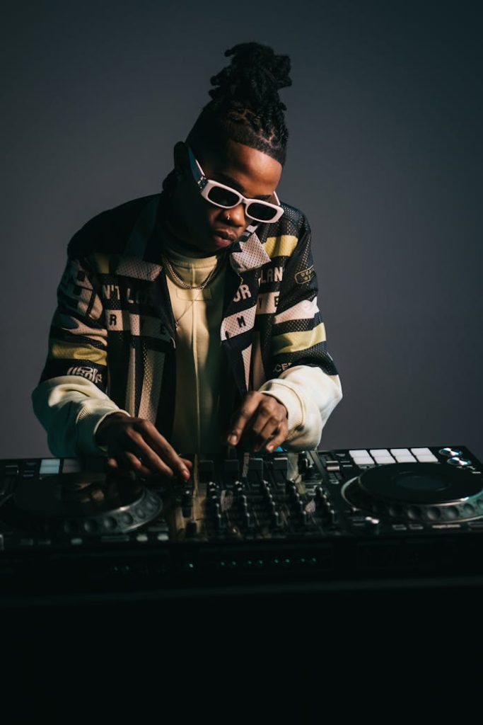 Young DJ with dreadlocks mixing tracks with a turntable in a modern studio setting.